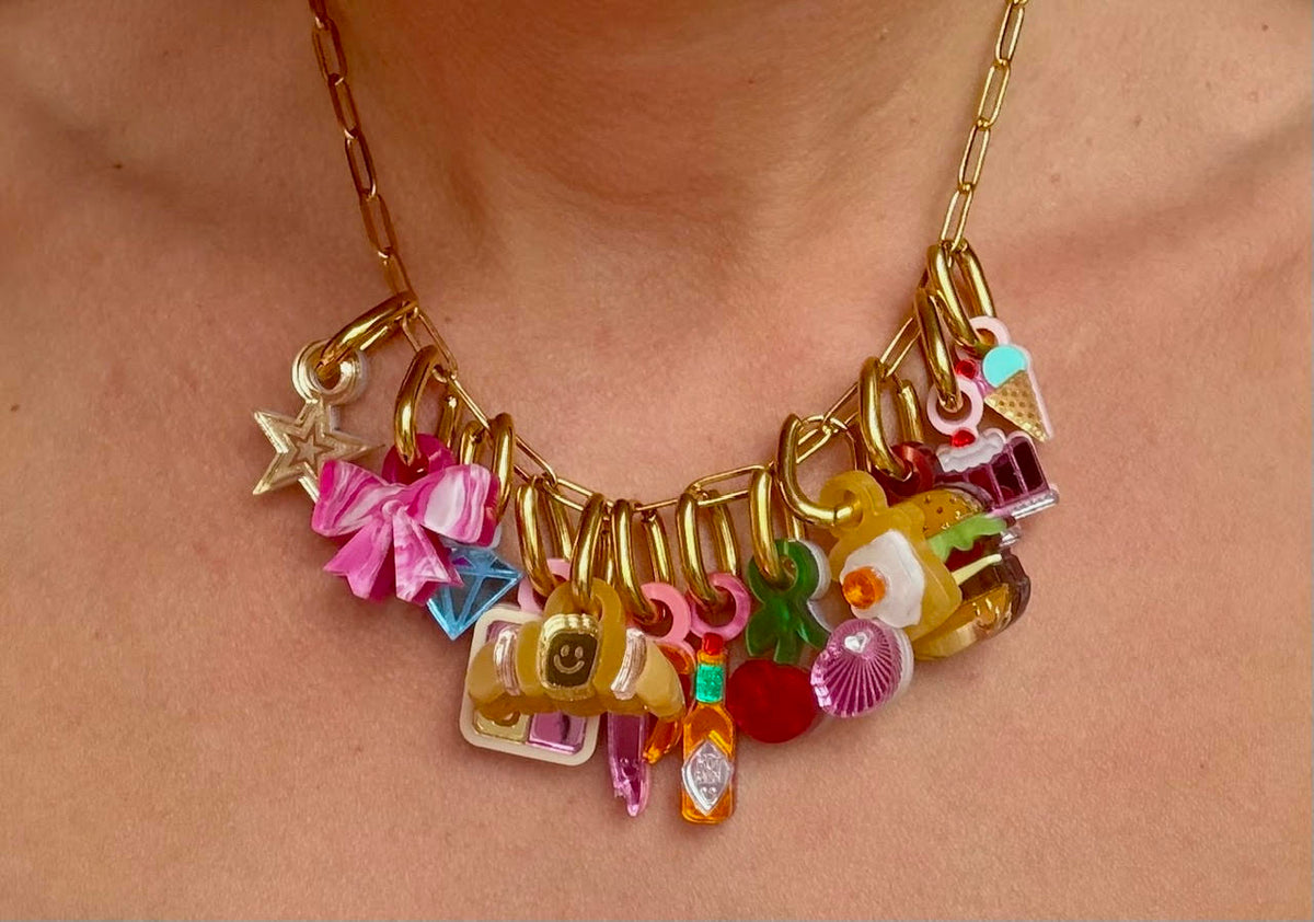 Gold chain necklace loaded with food charms including a burger, croissant, ice cream and hot sauce, styled as a snack stack